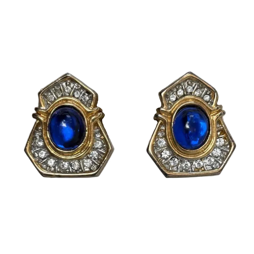 A pair of vintage gold-tone earrings featuring oval blue cabochon gemstones surrounded by clear crystal accents, set against a plain white background.