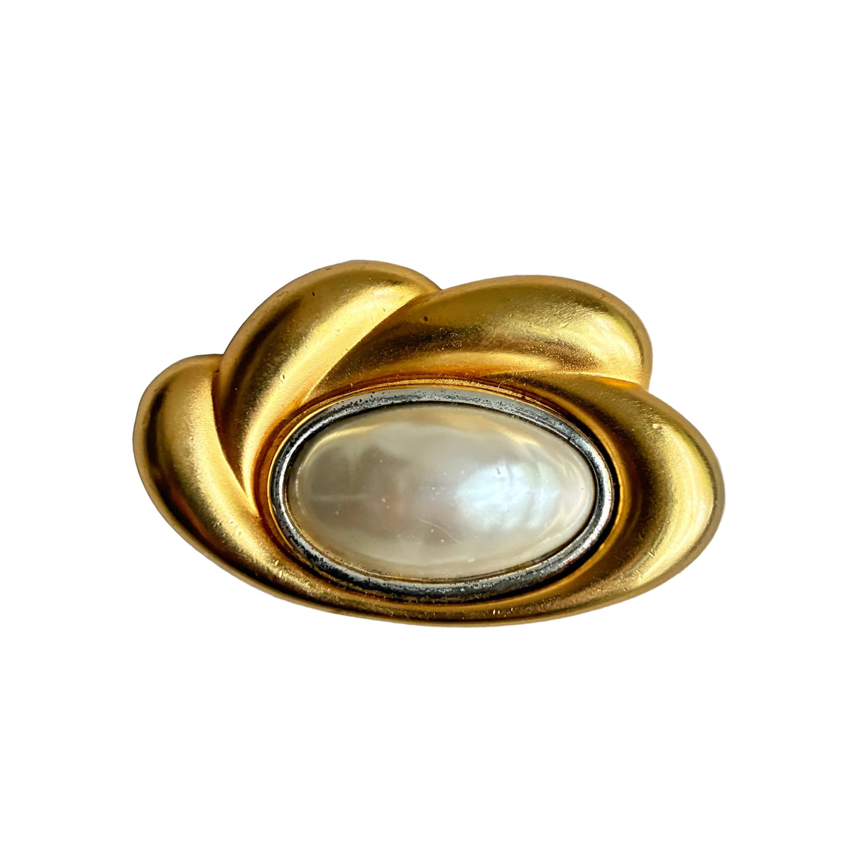 A vintage gold-tone cloud-shaped brooch featuring a central oval white pearl bezel-set in a silver-tone frame, photographed on a textured light gray background.