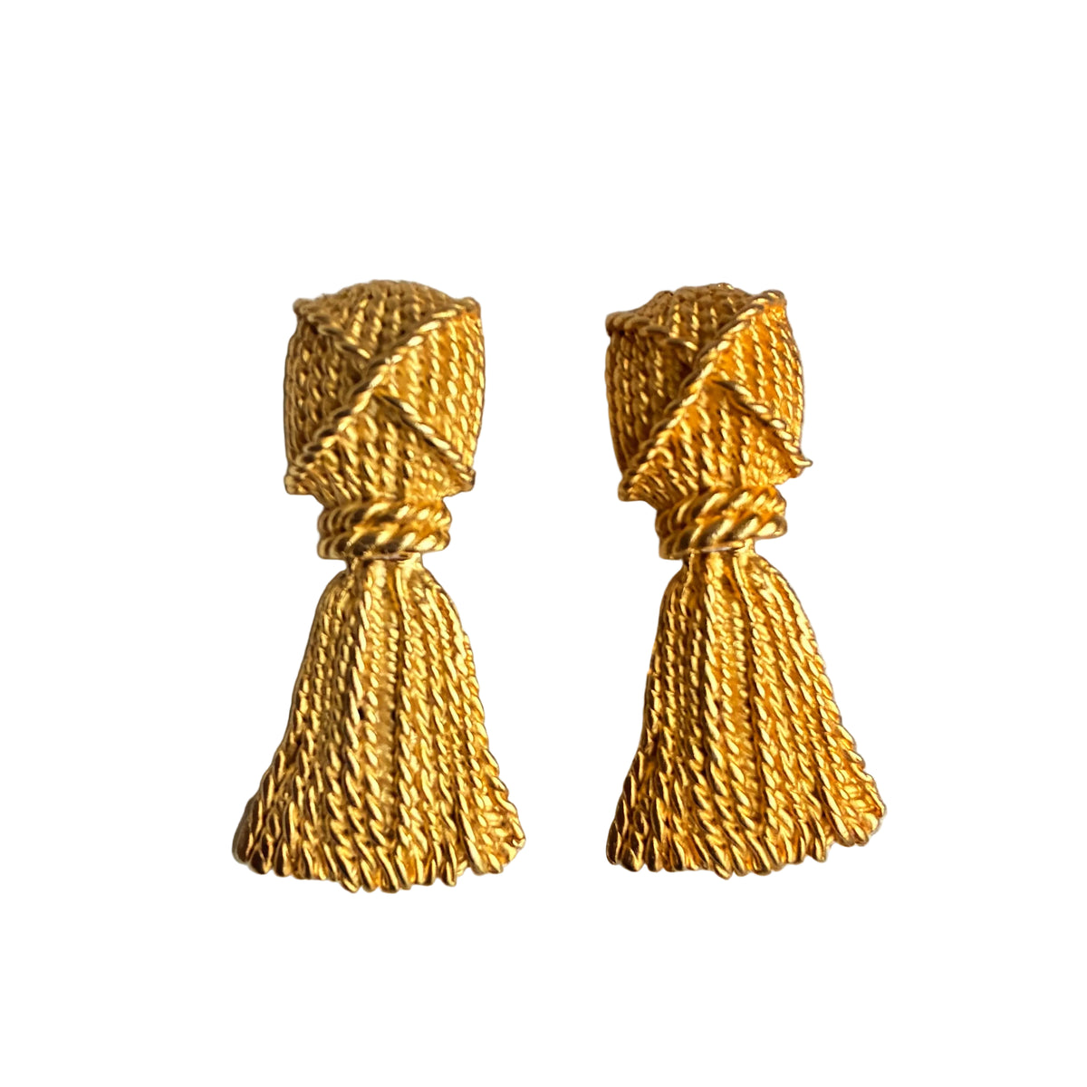 A pair of gold-toned tassel earrings with textured woven tops, displayed on a neutral beige fabric jewelry stand.