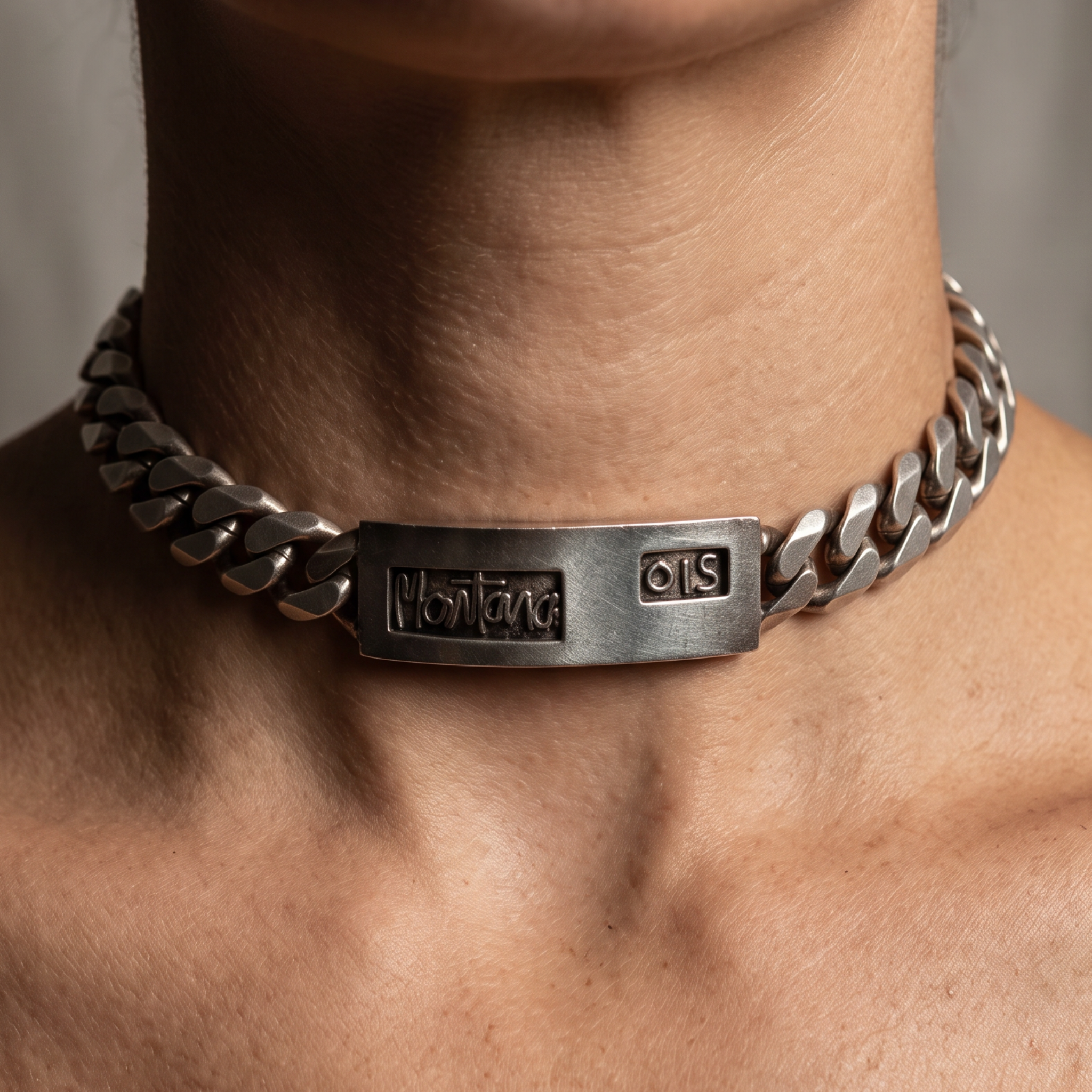 A close-up of a person's neck and upper chest wearing a chunky silver chain choker with a rectangular engraved plate.