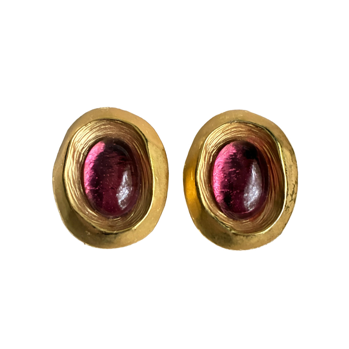 A pair of gold oval stud earrings with faceted gold edges and oval pinkish-red cabochon centers, displayed on a white textured jewelry roll.